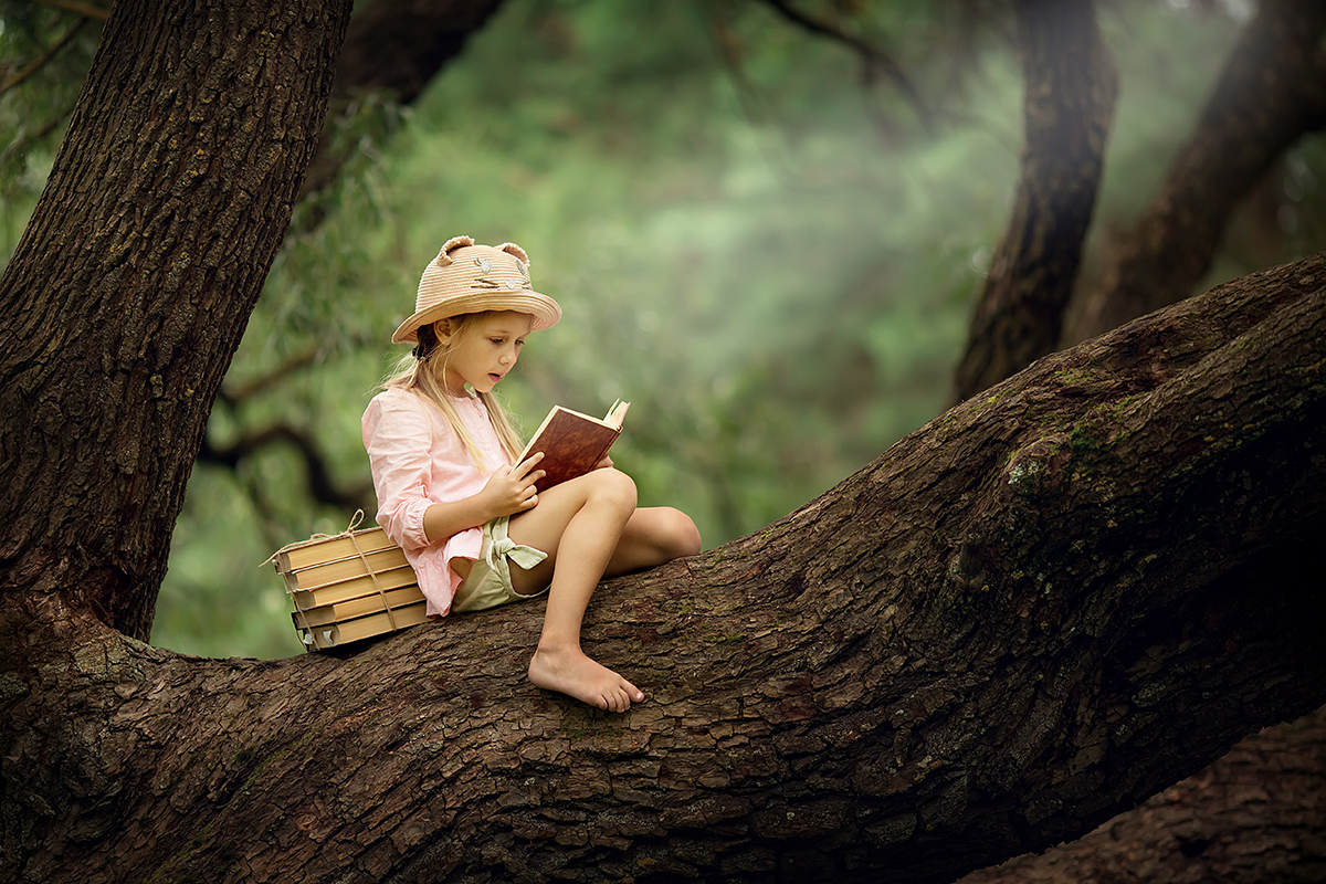 A girl reads a book while sitting in a tree.